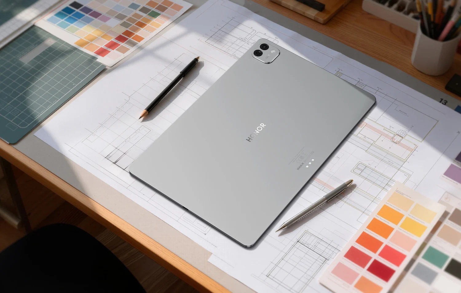 HONOR MagicPad4 in grey placed face down alongside a pen and printed color samples.